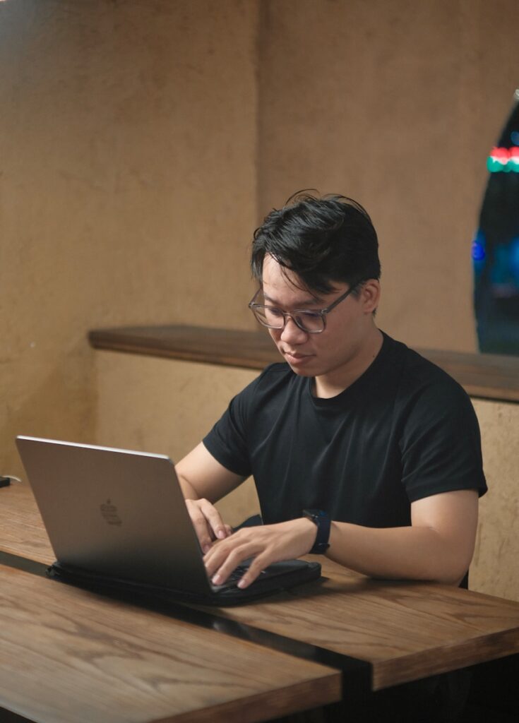 Man in black t-shirt working on laptop at table