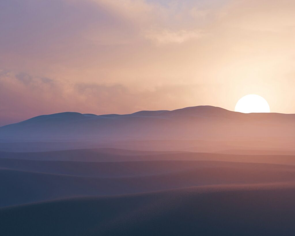 Sun setting behind hazy desert mountains at dusk