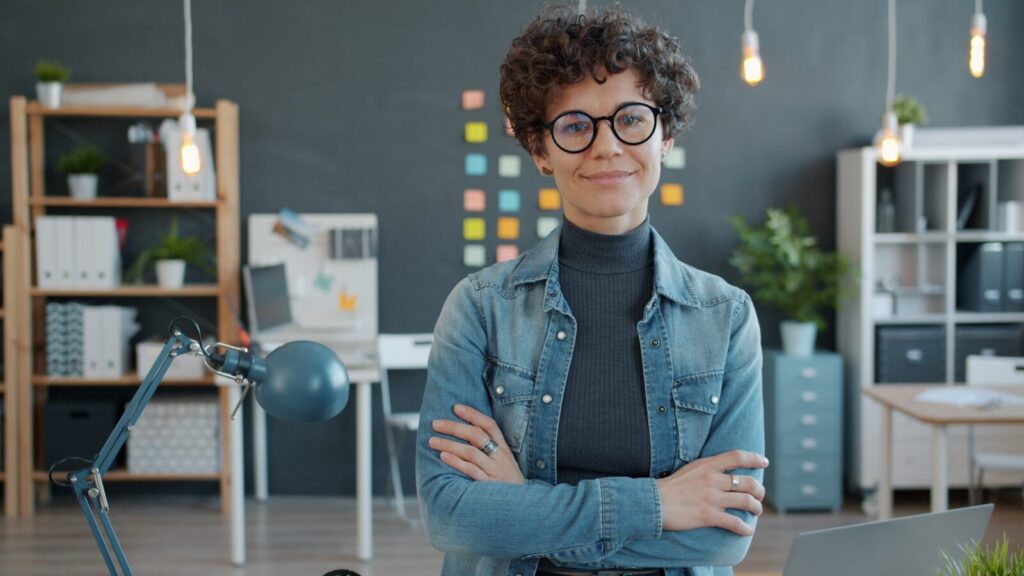 A woman with glasses smiles in an office.